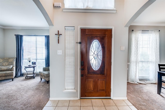 entrance foyer featuring light tile patterned floors, arched walkways, light carpet, baseboards, and crown molding