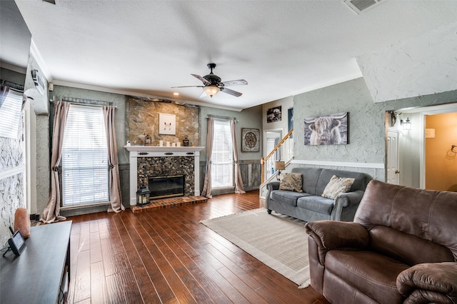 living room featuring dark wood-style flooring, a fireplace, visible vents, ornamental molding, and stairs