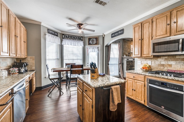 kitchen featuring stainless steel appliances, visible vents, ornamental molding, a kitchen island, and light stone countertops