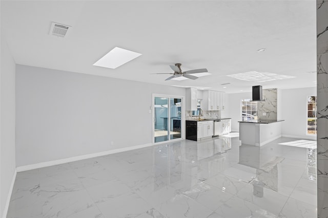 unfurnished living room with ceiling fan and a skylight