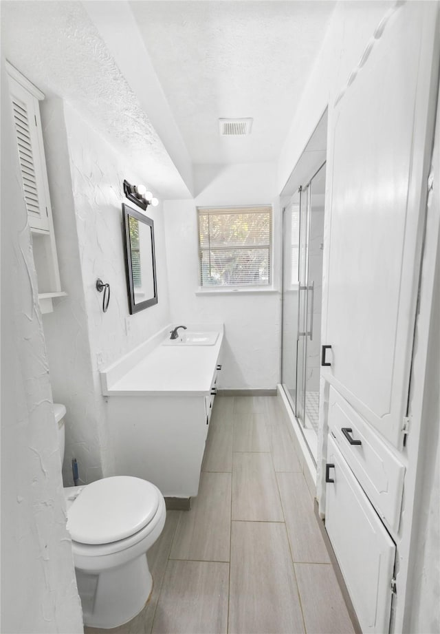 bathroom featuring vanity, a shower with shower door, a textured ceiling, and toilet