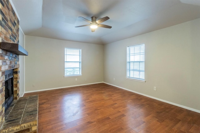 unfurnished living room with a brick fireplace, plenty of natural light, dark wood-type flooring, and ceiling fan