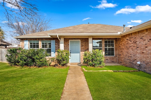 view of front of house featuring roof with shingles, brick siding, a lawn, and fence