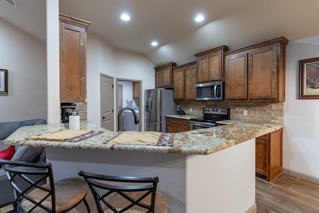 kitchen featuring stainless steel appliances, light stone countertops, a kitchen bar, and kitchen peninsula