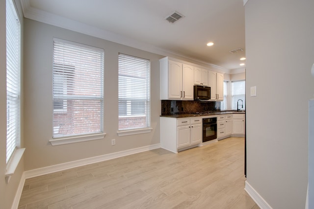 kitchen with white cabinets, decorative backsplash, black appliances, a healthy amount of sunlight, and light hardwood / wood-style flooring