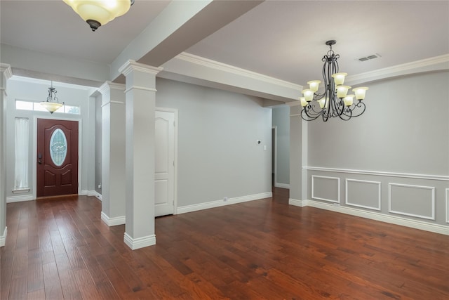 entryway featuring dark wood-type flooring, ornamental molding, a chandelier, and decorative columns