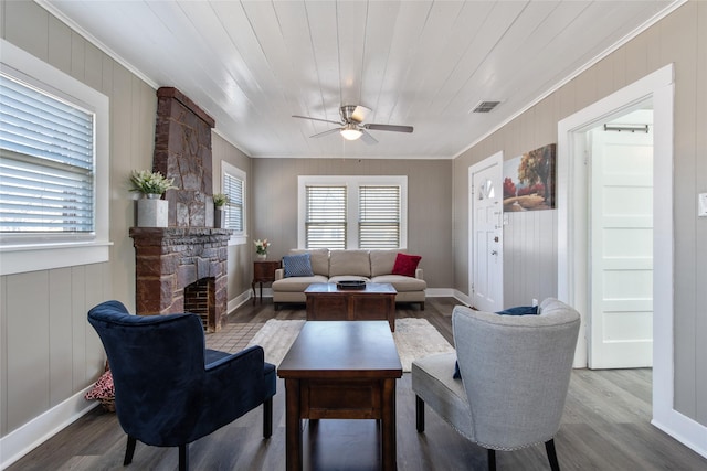 living room with a stone fireplace, light hardwood / wood-style flooring, ornamental molding, and wooden ceiling