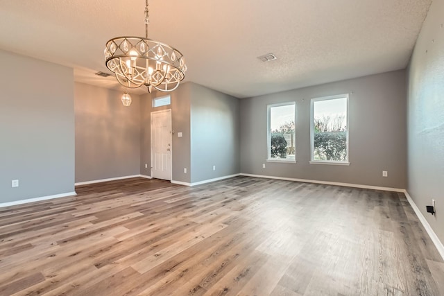 unfurnished room featuring an inviting chandelier, a textured ceiling, and hardwood / wood-style flooring