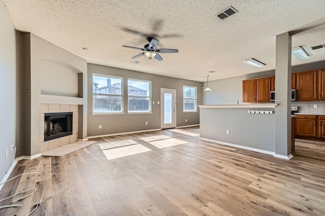 unfurnished living room featuring a textured ceiling, light hardwood / wood-style floors, a tile fireplace, and ceiling fan