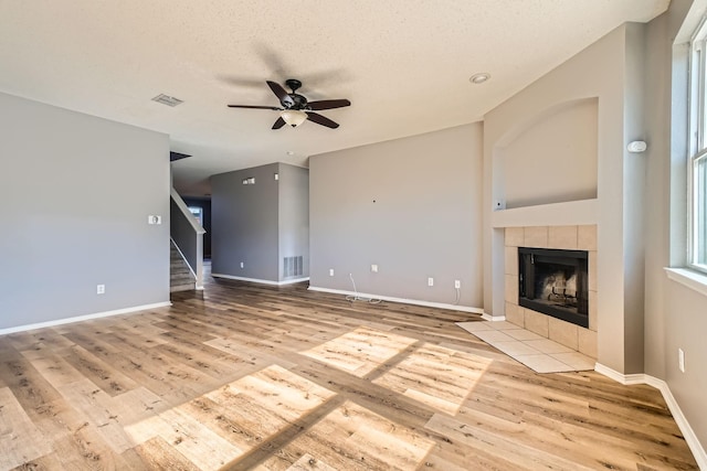 unfurnished living room with ceiling fan, light wood-type flooring, a textured ceiling, and a fireplace