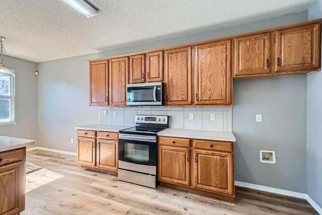 kitchen with tasteful backsplash, appliances with stainless steel finishes, light wood-type flooring, and decorative light fixtures