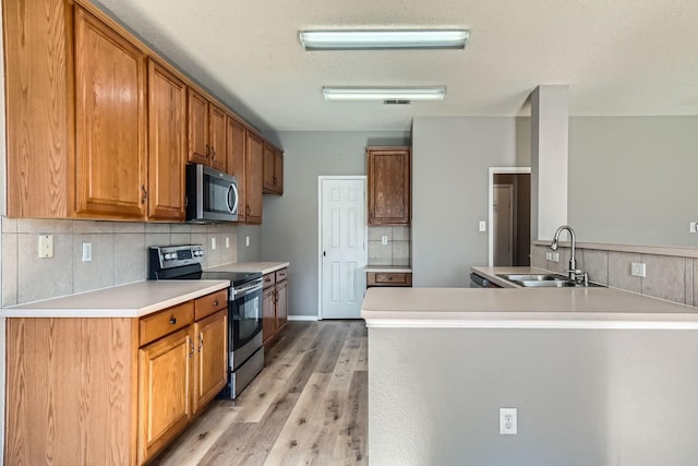 kitchen featuring tasteful backsplash, sink, kitchen peninsula, stainless steel appliances, and light wood-type flooring