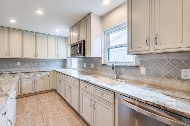 kitchen with light stone counters, sink, decorative backsplash, and stainless steel appliances