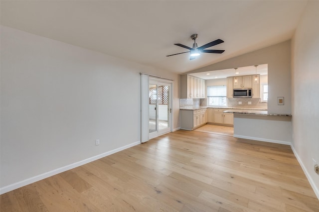 kitchen featuring vaulted ceiling, light wood-type flooring, kitchen peninsula, ceiling fan, and backsplash