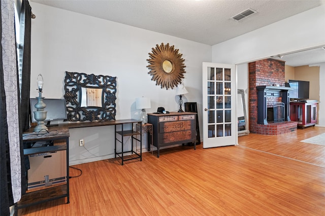 interior space with a textured ceiling, a fireplace, french doors, and wood-type flooring