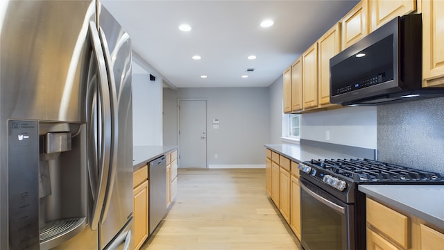 kitchen featuring appliances with stainless steel finishes, light brown cabinetry, light hardwood / wood-style flooring, and backsplash