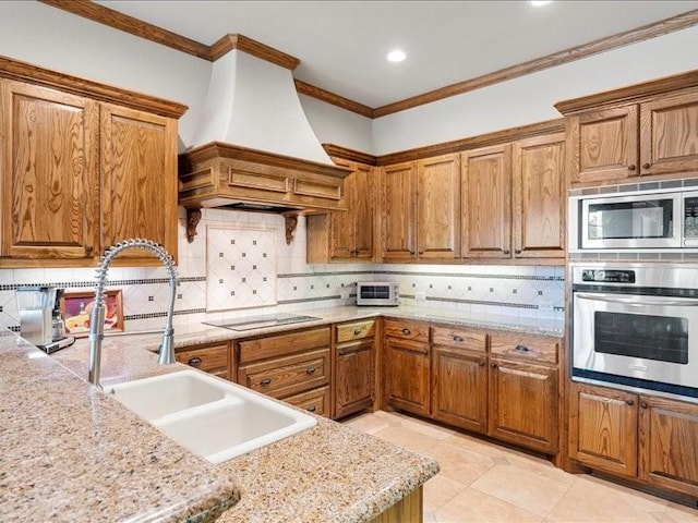 kitchen with brown cabinets, custom exhaust hood, stainless steel appliances, and light stone counters