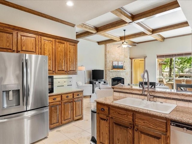 kitchen with coffered ceiling, appliances with stainless steel finishes, open floor plan, a stone fireplace, and a sink