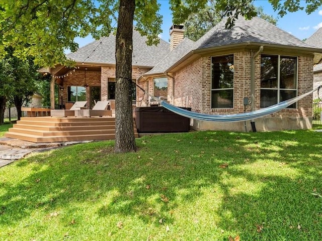 rear view of property with brick siding, a chimney, a lawn, a jacuzzi, and a wooden deck