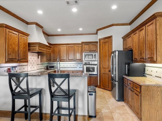 kitchen featuring tasteful backsplash, a kitchen bar, dark stone counters, stainless steel appliances, and custom range hood