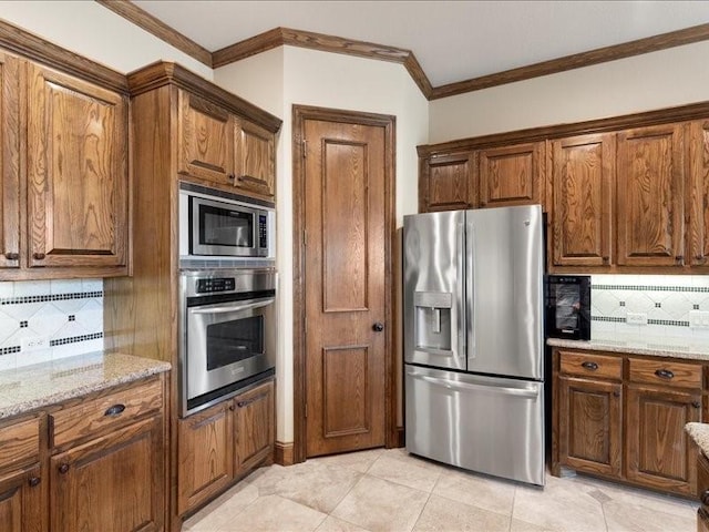 kitchen with light stone counters, appliances with stainless steel finishes, tasteful backsplash, brown cabinetry, and crown molding