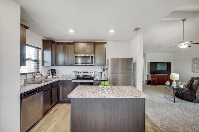 kitchen featuring sink, stainless steel appliances, a center island, dark brown cabinetry, and light stone countertops