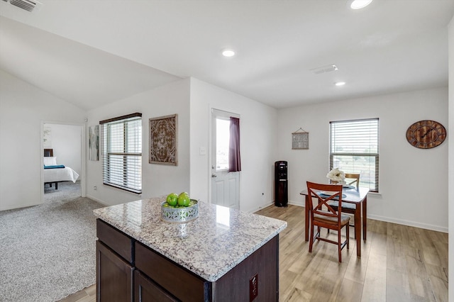 kitchen with dark brown cabinetry, light stone countertops, lofted ceiling, and a kitchen island