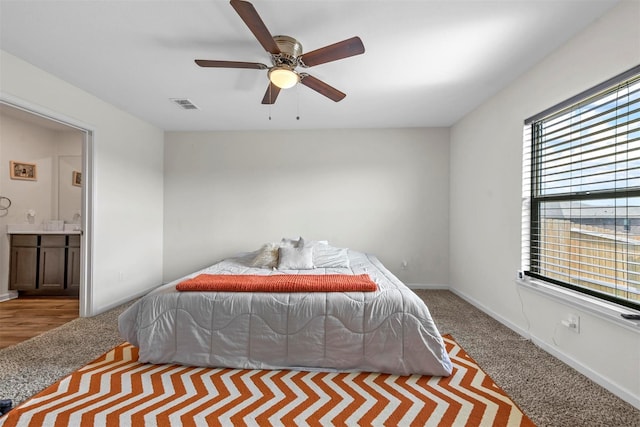 bedroom with ceiling fan, light colored carpet, and connected bathroom