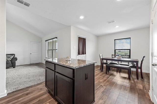 kitchen featuring dark brown cabinetry, light stone counters, wood-type flooring, a kitchen island, and vaulted ceiling