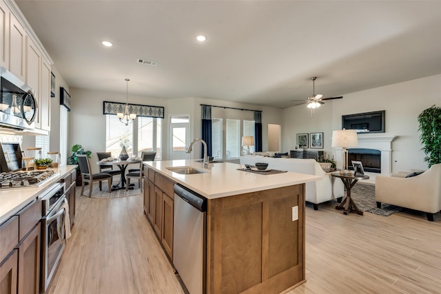 kitchen with appliances with stainless steel finishes, decorative light fixtures, sink, a center island with sink, and light hardwood / wood-style flooring