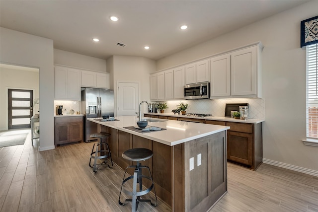 kitchen featuring a center island with sink, light wood-type flooring, a kitchen breakfast bar, stainless steel appliances, and white cabinets