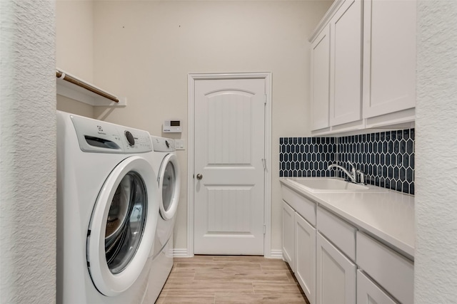 washroom featuring cabinets, sink, washing machine and dryer, and light hardwood / wood-style flooring