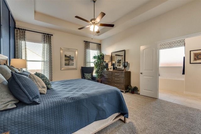 bedroom with ceiling fan, light colored carpet, a tray ceiling, and multiple windows