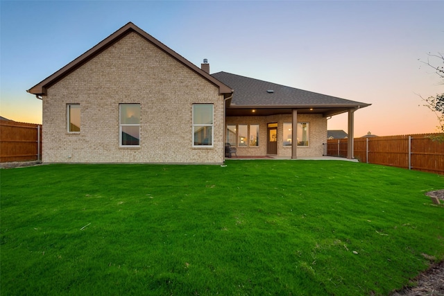 back house at dusk featuring a yard and a patio area