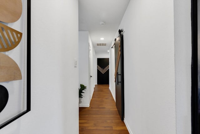 corridor featuring dark wood-type flooring and a barn door