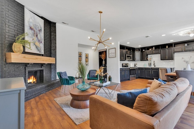 living room with sink, an inviting chandelier, a fireplace, and light hardwood / wood-style flooring