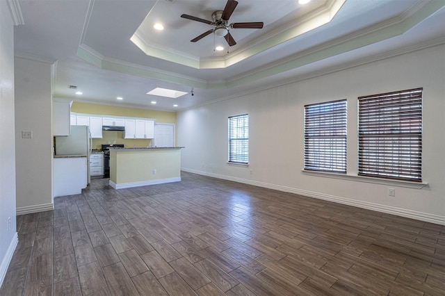 unfurnished living room featuring a skylight, dark wood-type flooring, a raised ceiling, and ceiling fan