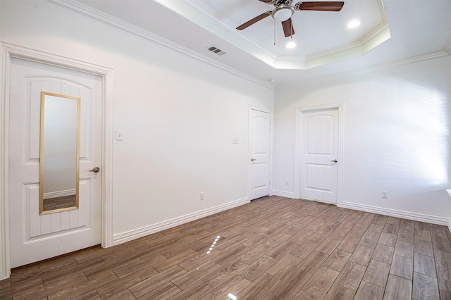 empty room featuring wood-type flooring, ornamental molding, ceiling fan, and a tray ceiling