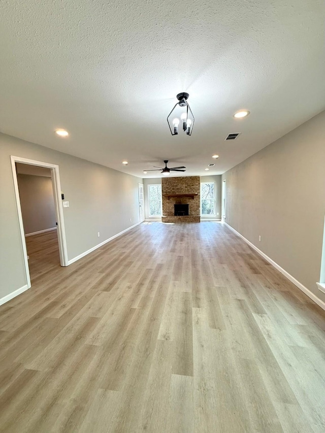 unfurnished living room featuring a brick fireplace, light hardwood / wood-style flooring, a textured ceiling, and ceiling fan