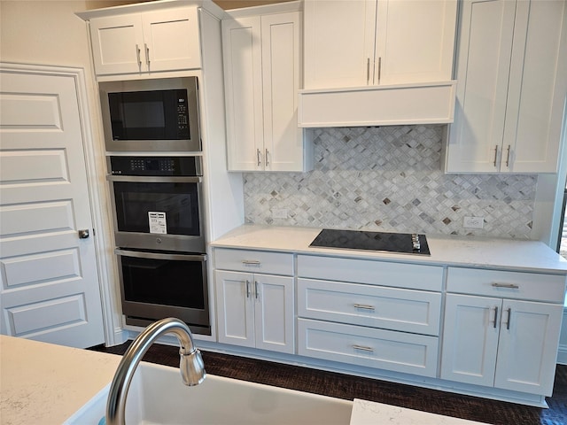 kitchen featuring white cabinetry, stainless steel double oven, light stone counters, and black electric cooktop