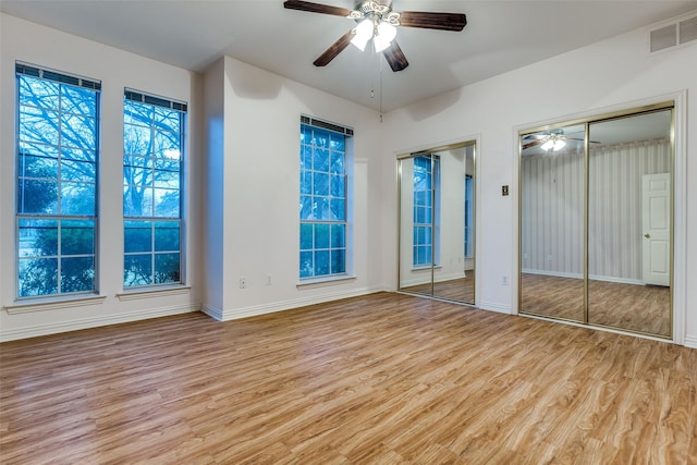 unfurnished bedroom featuring ceiling fan, two closets, and light wood-type flooring