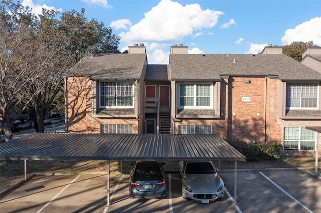 rear view of house featuring brick siding, a shingled roof, a chimney, and covered and uncovered parking