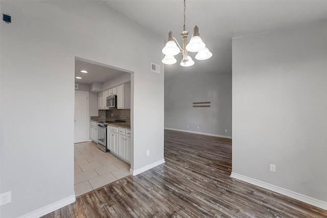 kitchen with white cabinetry, wood-type flooring, decorative backsplash, stainless steel appliances, and an inviting chandelier