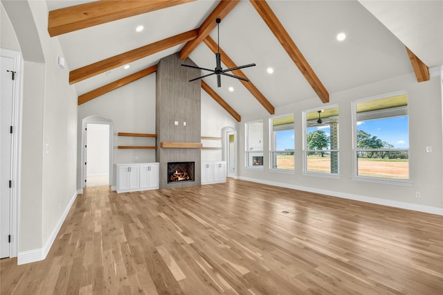 unfurnished living room with high vaulted ceiling, a fireplace, ceiling fan, light hardwood / wood-style floors, and beam ceiling