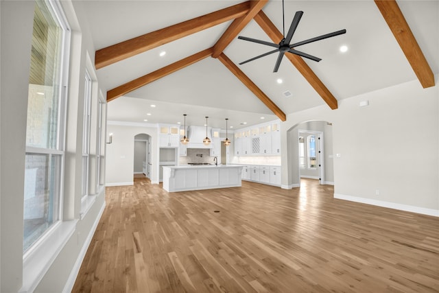 unfurnished living room with beamed ceiling, ceiling fan, high vaulted ceiling, and light wood-type flooring