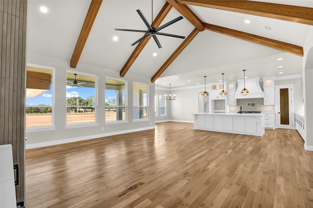 unfurnished living room with beam ceiling, ceiling fan with notable chandelier, and light wood-type flooring