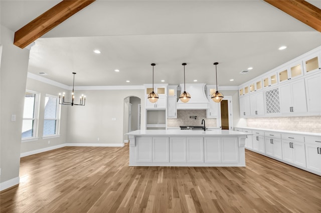 kitchen with white cabinetry, hanging light fixtures, sink, and an island with sink