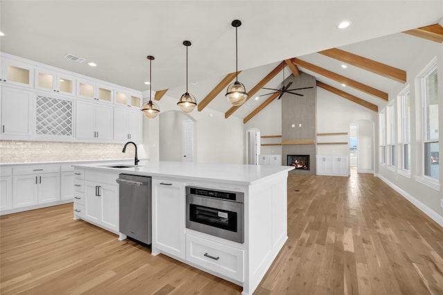 kitchen with white cabinetry, stainless steel appliances, a center island with sink, decorative light fixtures, and light wood-type flooring