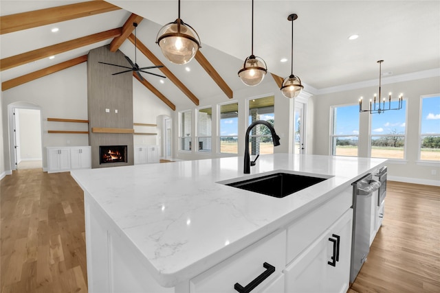 kitchen with pendant lighting, sink, a kitchen island with sink, white cabinetry, and light stone countertops