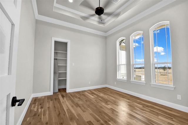 unfurnished bedroom with hardwood / wood-style flooring, ceiling fan, a tray ceiling, crown molding, and a closet